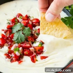 A tortilla chip in a pan of white queso dip.