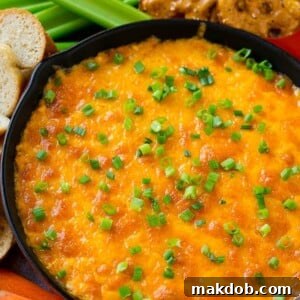 Buffalo ranch chicken dip topped with melted cheese and green onions, surrounded by vegetables, pretzels and baguette slices.