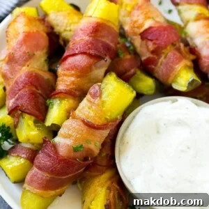 Bacon wrapped pickles on a plate with a side of creamy ranch dressing, a unique savory snack.