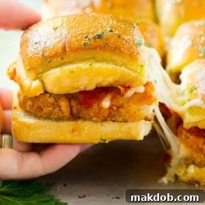 A crispy chicken sandwich being pulled away by a hand, showcasing the delicious filling of chicken parmesan sliders.