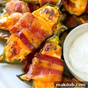 A plate of bacon wrapped jalapeno poppers served with ranch dressing.