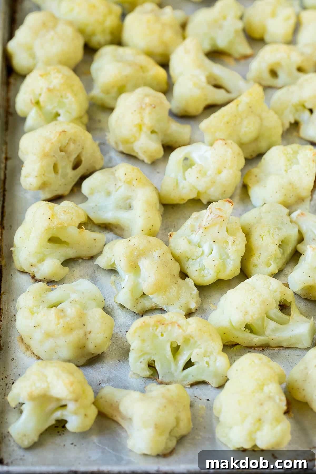 Battered and cooked cauliflower florets evenly spread out on a baking pan, showing their crispy texture before being coated in sauce.