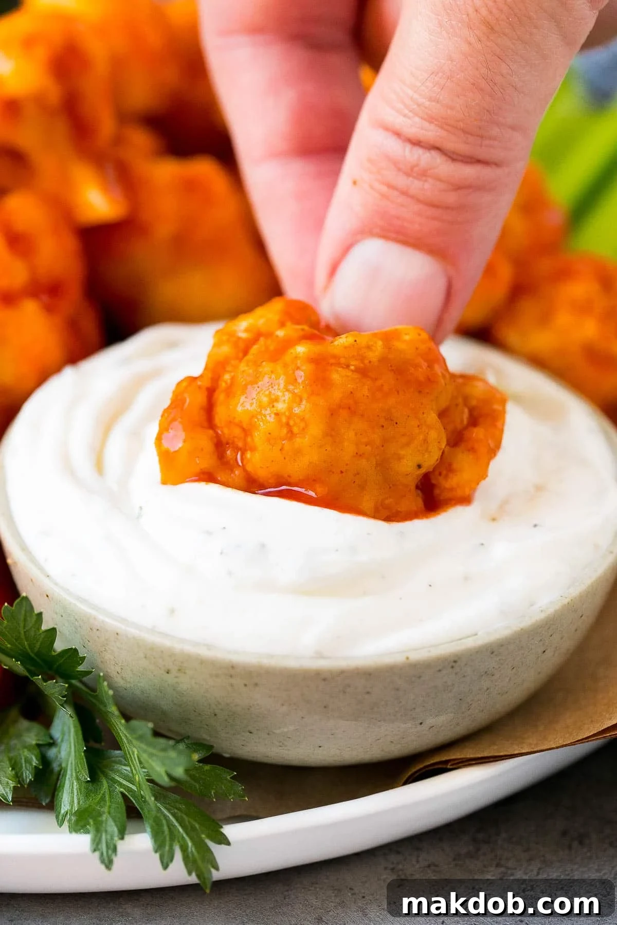 A hand dipping a piece of buffalo cauliflower into a bowl of creamy ranch dip, emphasizing its snackable quality.