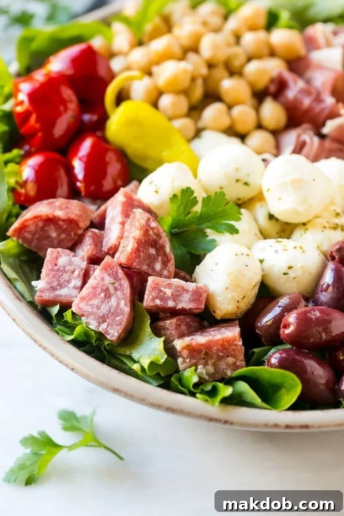 Antipasto Salad Recipe | Italian Salad | Main Course Salad | Antipasto Recipe #salad #salami #italianfood #dinner #lunch #dinneratthezoo A large bowl of fresh mixed greens topped generously with a colorful array of antipasto salad ingredients including assorted Italian meats, fresh mozzarella, chickpeas, and various marinated vegetables, waiting to be tossed with dressing.