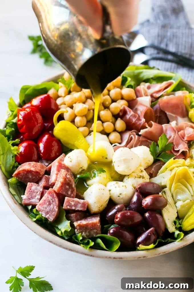 Antipasto Salad Recipe | Italian Salad | Main Course Salad | Antipasto Recipe #salad #salami #italianfood #dinner #lunch #dinneratthezoo A stream of homemade zesty dressing being poured from a pitcher over a fresh and colorful Antipasto salad, ready for serving.