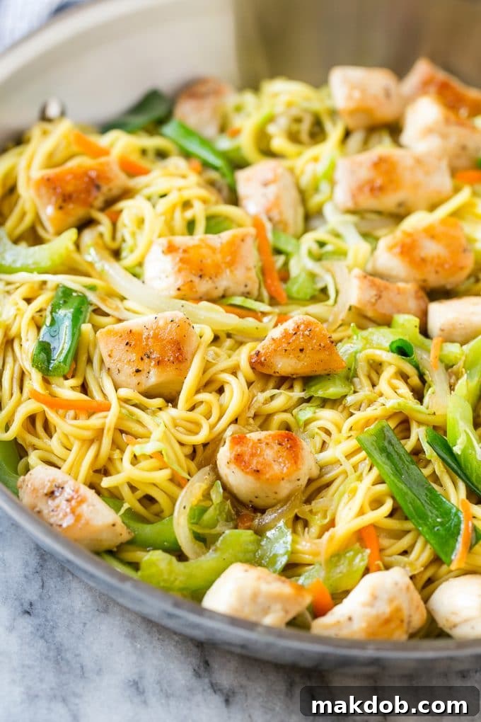 Chicken chow mein sizzling in a large skillet with noodles and colorful mixed vegetables.