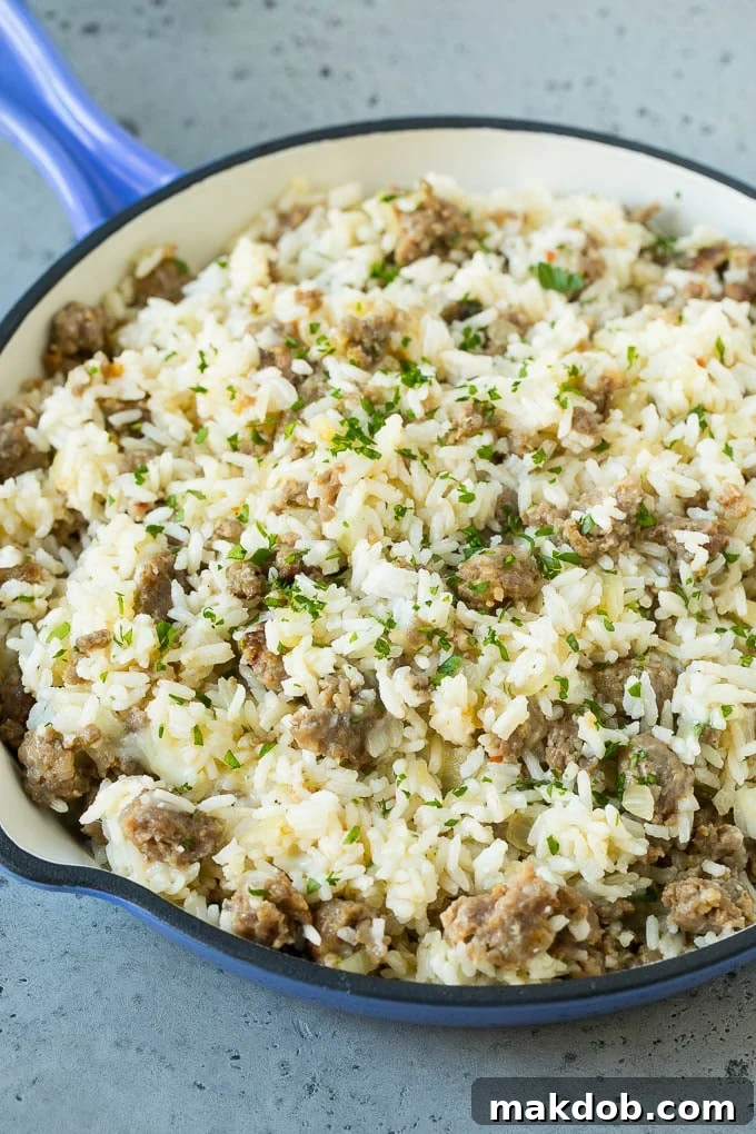 A mixture of cooked rice, Italian sausage, diced onions, garlic, and shredded cheese being prepared in a skillet.