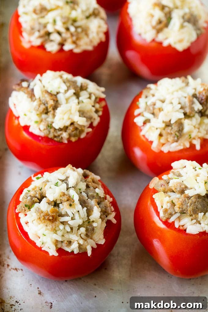 Hollowed out tomatoes on a baking sheet, ready to be stuffed with a savory mixture of sausage and rice.