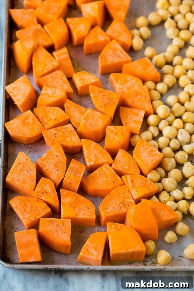 Raw sweet potatoes and canned chickpeas on a sheet pan.