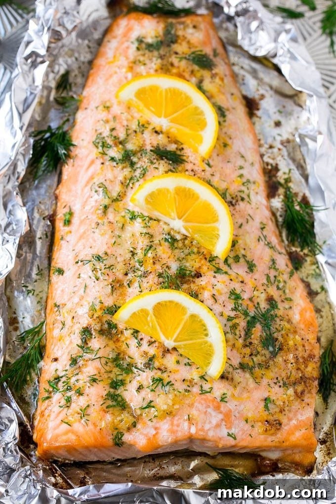 Salmon in foil topped with butter, garlic, dill and lemon slices, ready to be baked.