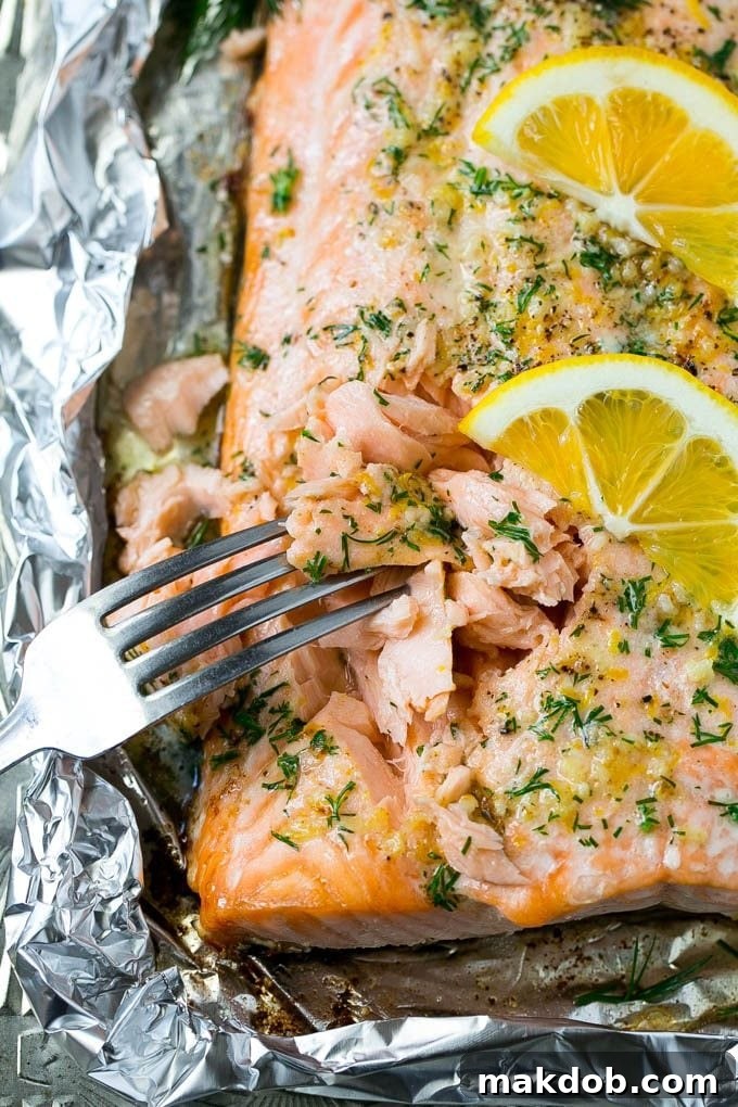 A fork cutting into a salmon filet that's been cooked in foil with garlic and herbs, showcasing its flaky texture.
