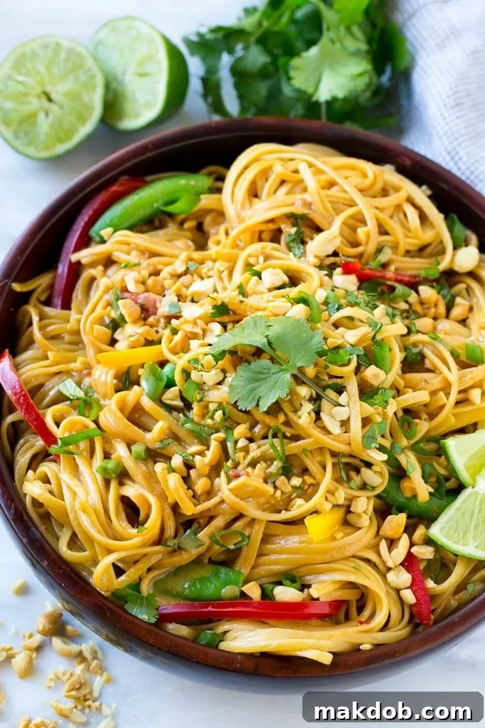A communal serving bowl filled with a generous portion of Thai peanut noodles, garnished with a sprinkle of fresh chopped peanuts, vibrant green cilantro, and thinly sliced green onions, showcasing the dish's appealing texture and color.