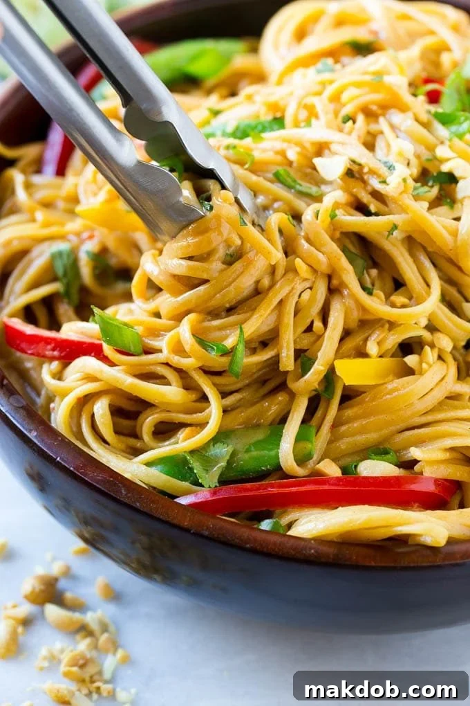 Creamy Thai Peanut Noodles 4 Tongs serving up a portion of Thai peanut noodles, illustrating the perfect consistency and how the sauce coats the noodles.