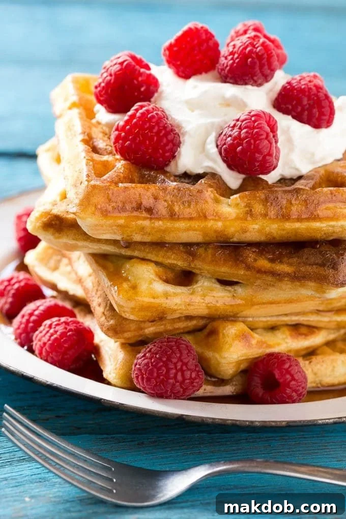 Dreamy Overnight Yeast Waffles 4 Golden brown yeast waffles piled high, drizzled with maple syrup and topped with whipped cream and fresh mixed berries, ready for a delicious breakfast.