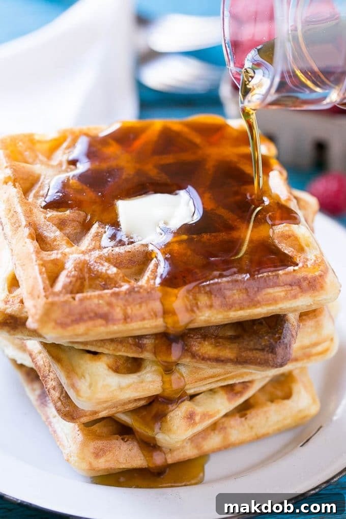 Dreamy Overnight Yeast Waffles 5 A perfectly cooked stack of golden yeast waffles, generously topped with a pat of melting butter and glistening maple syrup, ready to be enjoyed.