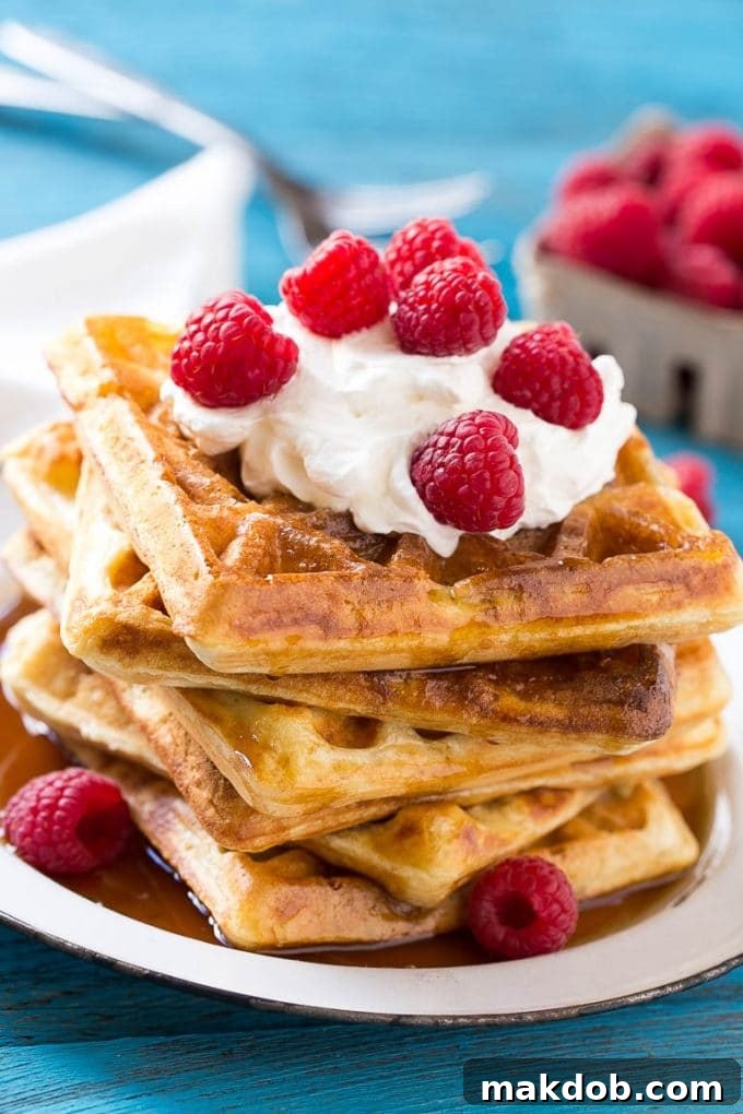 Dreamy Overnight Yeast Waffles 6 Overnight yeast waffles elegantly presented with swirls of whipped cream and a sprinkle of fresh raspberries, showcasing their appealing texture.