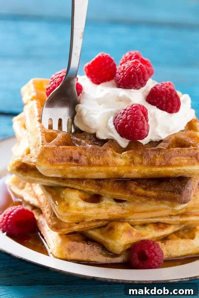 Dreamy Overnight Yeast Waffles 7 A fork piercing a soft stack of yeast raised waffles, revealing their fluffy and airy interior, highlighting the perfect texture.