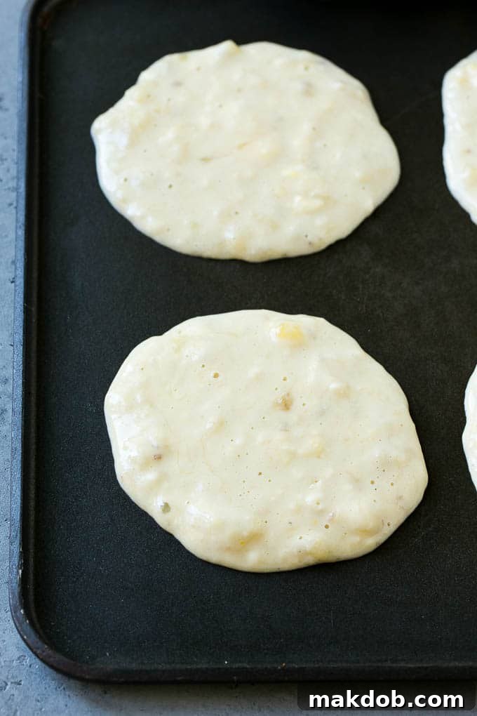 Cooking Banana Pancakes on a Skillet Banana pancakes sizzling on a non-stick skillet, turning golden brown as they cook.