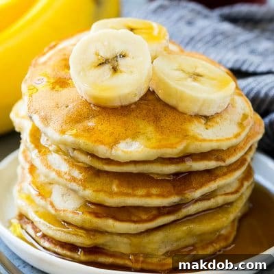 A stack of banana pancakes with banana slices and maple syrup.