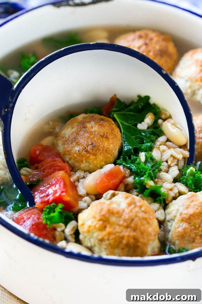 A ladle serving a generous portion of hearty farro soup, featuring perfectly cooked meatballs, white beans, and kale.