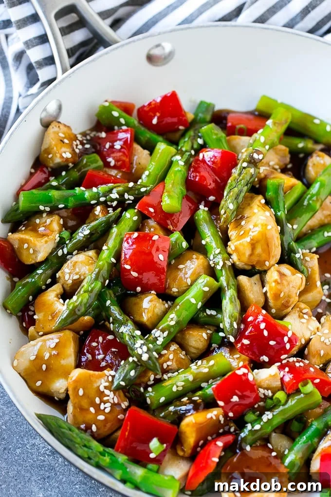 A pan of chicken teriyaki stir fry with chicken pieces, vibrant asparagus, and bright red peppers.