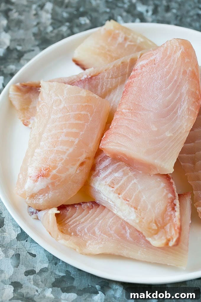 Tilapia fish fillets on a plate, ready for breading and frying for Baja fish tacos.