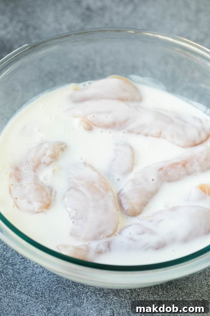 Buttermilk Marinated Chicken Tenders for Frying Chicken tenderloins soaking in a bowl of creamy buttermilk marinade.