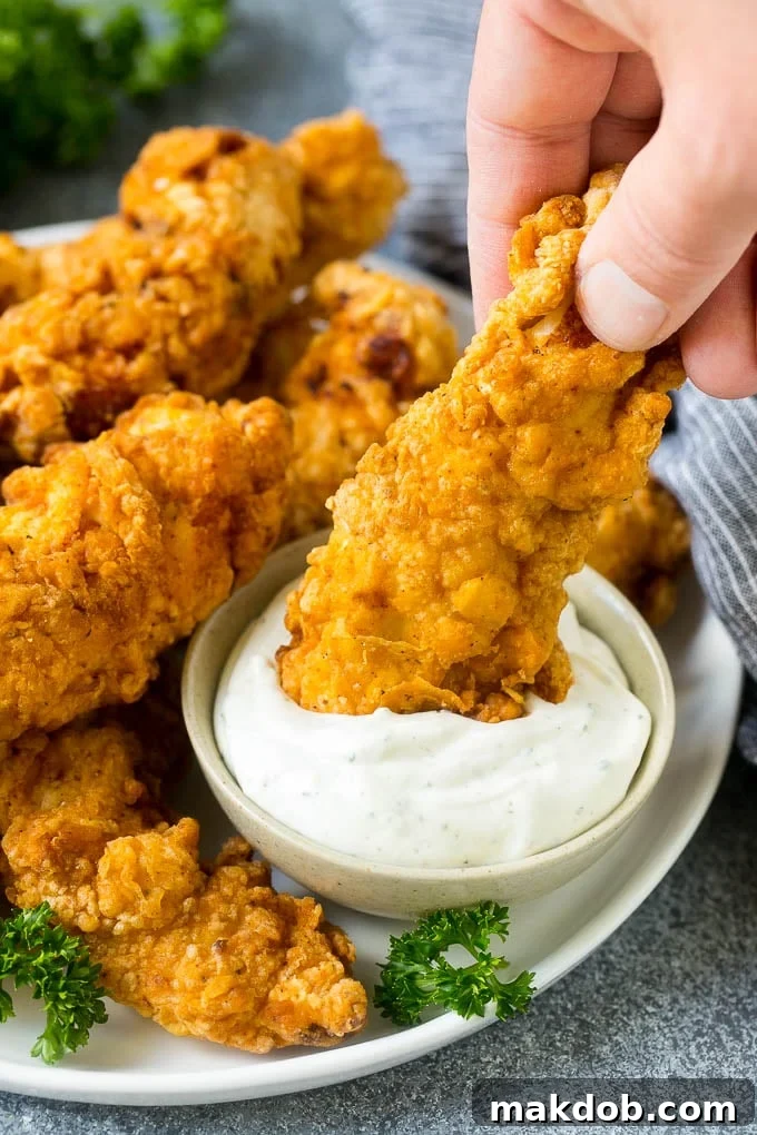 Chicken Finger with Ranch Dipping Sauce A crispy chicken finger being dipped into a bowl of creamy ranch sauce.