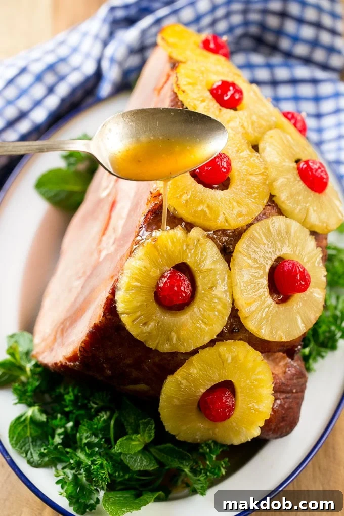 Pineapple Cherry Glazed Ham 4 A spoon pouring a sweet and savory glaze over a ham adorned with pineapple and cherries during baking.