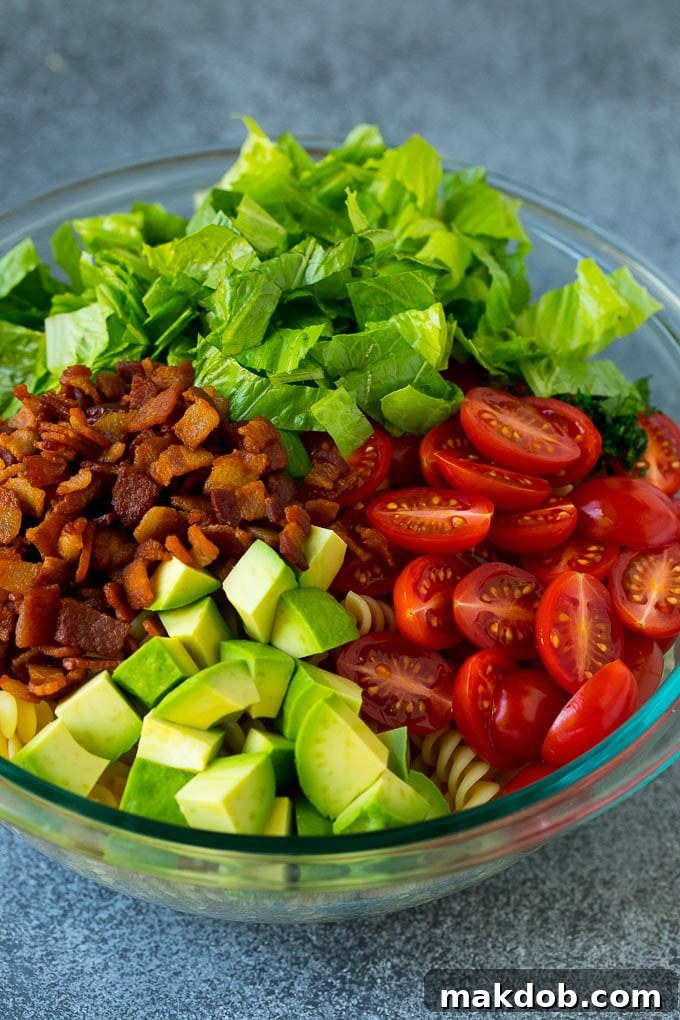 BLT Pasta Salad Recipe | Easy Pasta Salad | Bacon Pasta Salad #salad #pasta #blt #bacon #avocado #dinner #dinneratthezoo A large bowl filled with BLT pasta salad ingredients including bacon, lettuce, tomato, pasta, and avocado.