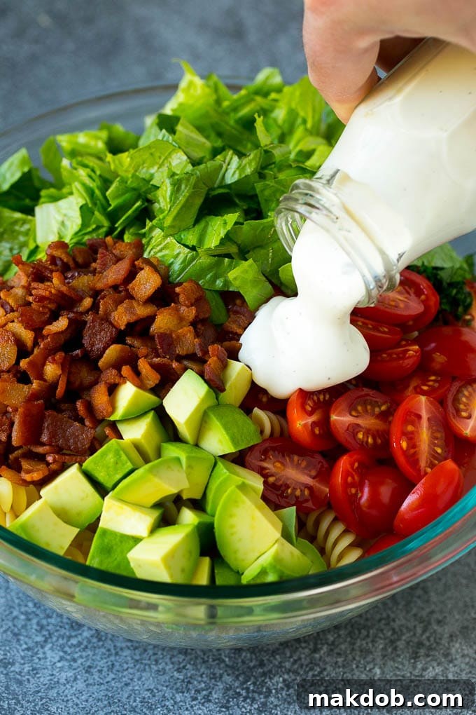 BLT Pasta Salad Recipe | Easy Pasta Salad | Bacon Pasta Salad #salad #pasta #blt #bacon #avocado #dinner #dinneratthezoo Creamy ranch dressing being drizzled over a mix of cherry tomatoes, shredded lettuce, crispy bacon, and diced avocado in a large bowl.