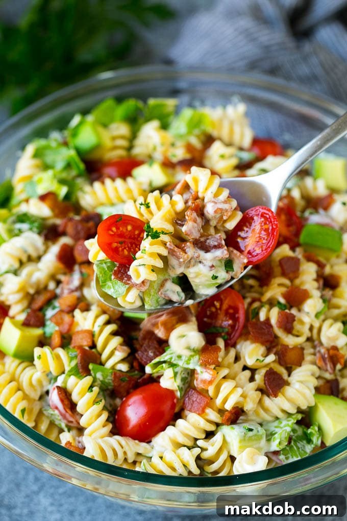 BLT Pasta Salad Recipe | Easy Pasta Salad | Bacon Pasta Salad #salad #pasta #blt #bacon #avocado #dinner #dinneratthezoo A serving spoon lifting a portion of BLT pasta salad, showcasing the pasta, bacon, lettuce, tomatoes, and avocado.