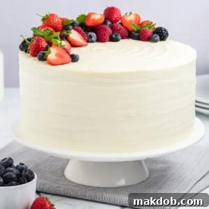 A berry chantilly cake on a cake stand, topped with fresh berries and mint sprigs.