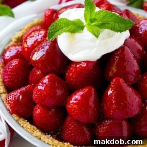 A pile of strawberries inside a graham cracker crust, topped with a shiny red glaze, whipped cream and mint.