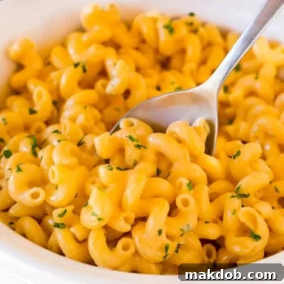 Slow cooker mac and cheese topped with parsley, with a serving spoon in it.