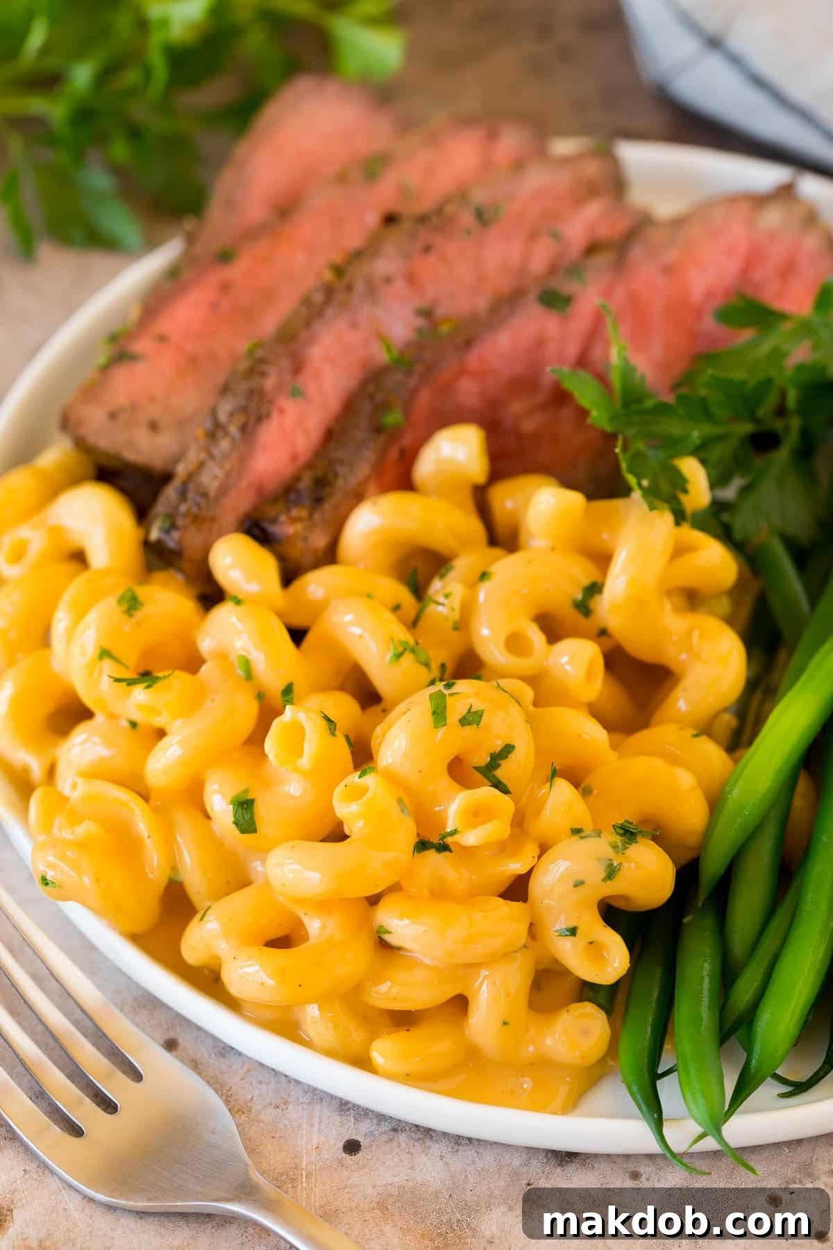 Slow cooker mac and cheese on a plate with sliced steak and vegetables.
