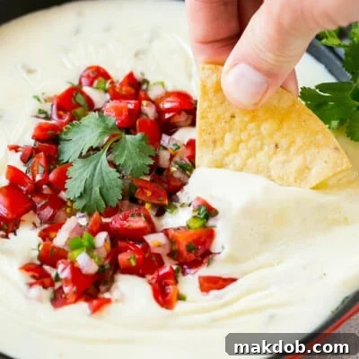 A tortilla chip in a pan of white queso dip.