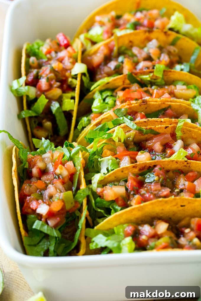 A pan full of baked beef tacos topped with salsa and lettuce.