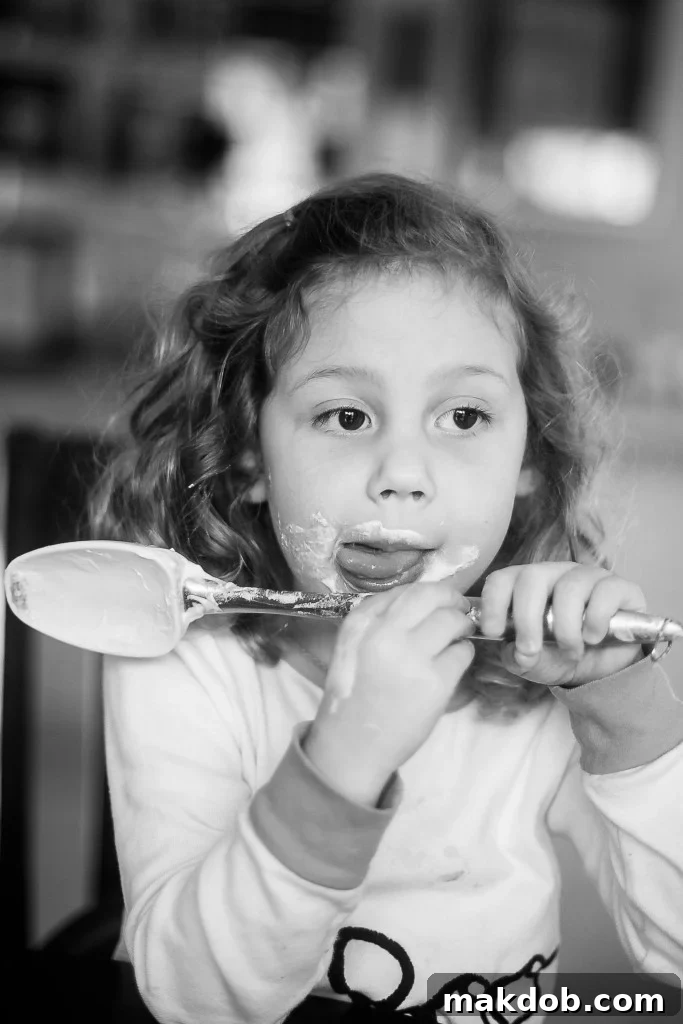 A child's hand holding a spoon, ready to lick the chocolate cake batter.