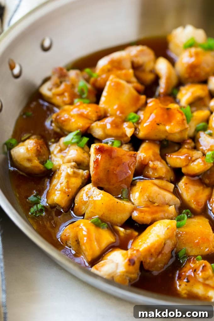 Bourbon chicken in a skillet coated in sauce and topped with green onions.