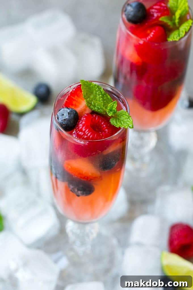 Two champagne flutes filled with sparkling berry champagne punch, garnished with fresh berries and a mint sprig, against a light background.