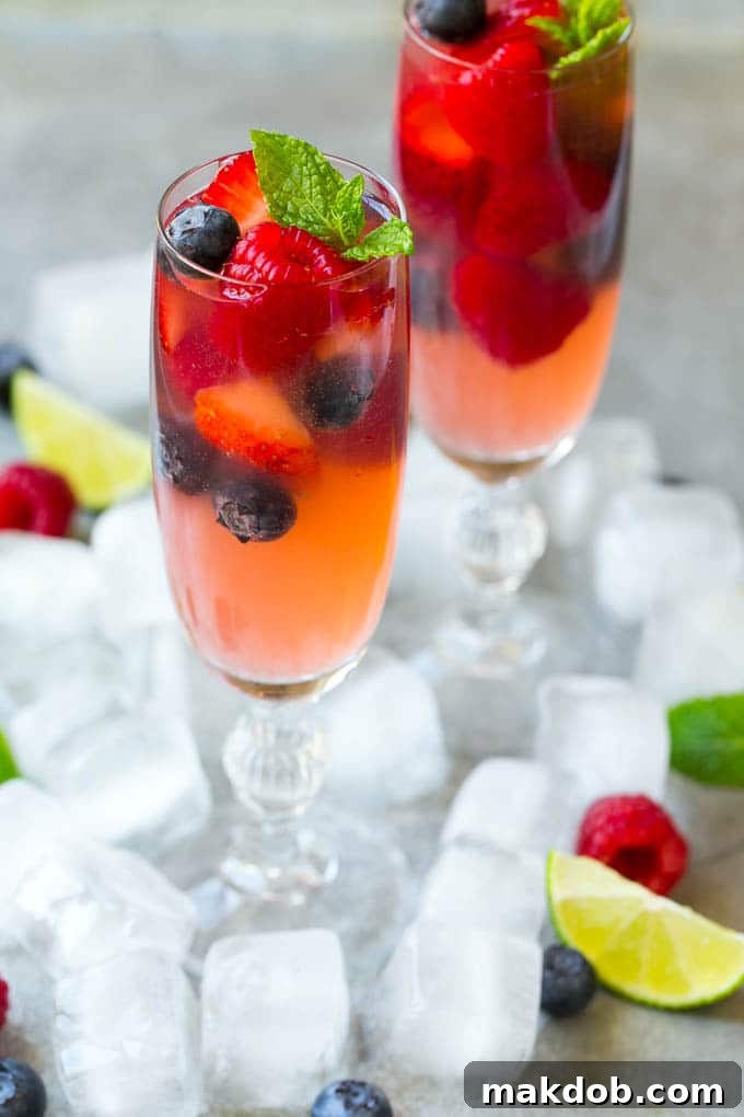 Two elegant champagne flutes filled with vibrant berry champagne punch, garnished with fresh berries, on a subtle background.