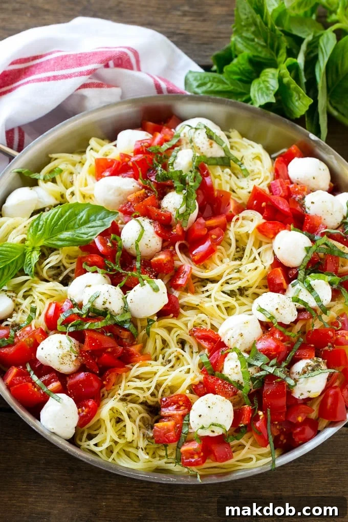 A pan of angel hair caprese pasta topped with olive oil, tomatoes, basil and fresh mozzarella.