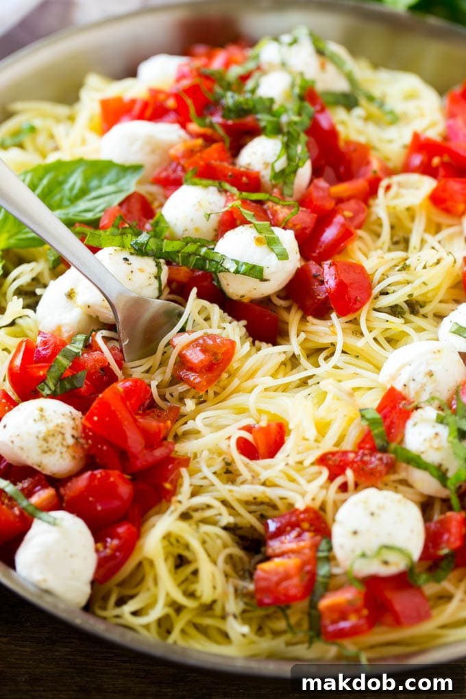 A pan of caprese pasta with angel hair pasta, olive oil, fresh basil, tomatoes and mozzarella cheese.
