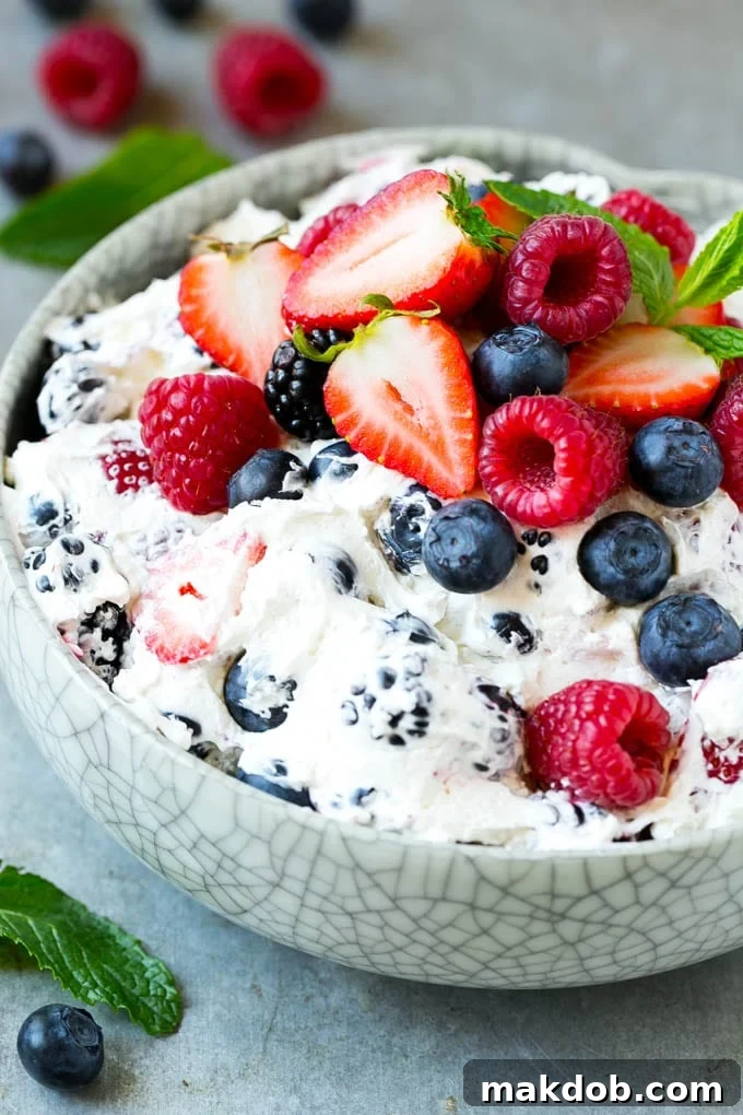 A serving bowl of creamy berry salad topped with blueberries, raspberries and strawberries.
