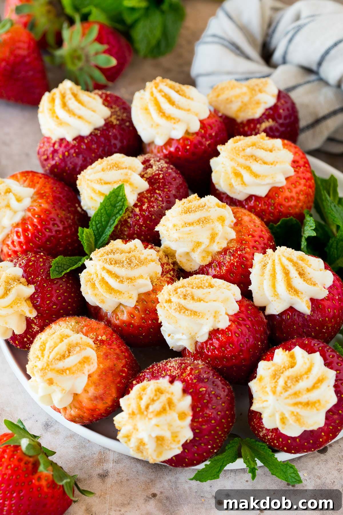 Strawberry Cheesecake Delights 2 A plate of cheesecake stuffed strawberries garnished with fresh mint, ready to be served as an elegant, no-bake dessert.