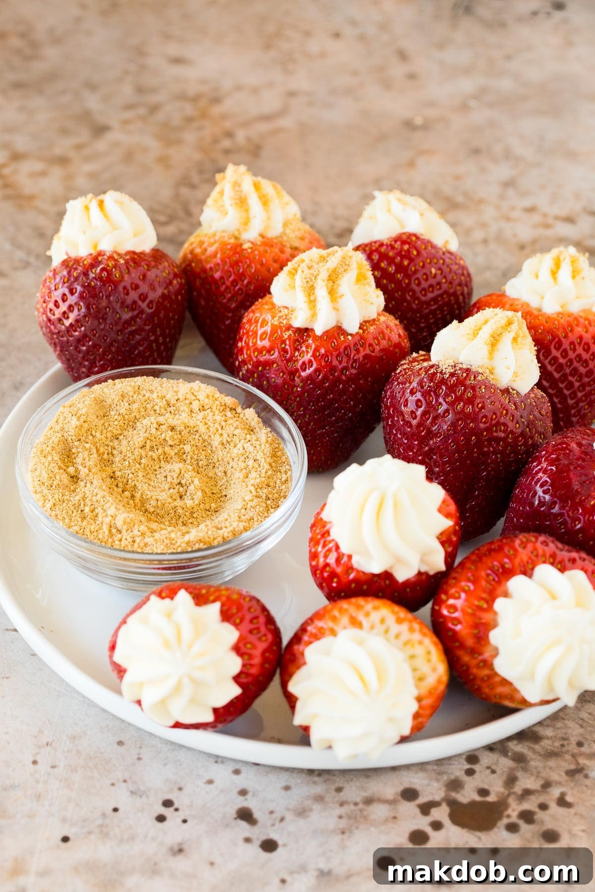 Strawberry Cheesecake Delights 5 A close-up of cheesecake-stuffed strawberries arranged on a plate next to a small bowl of graham cracker crumbs, highlighting the beautiful texture and presentation.