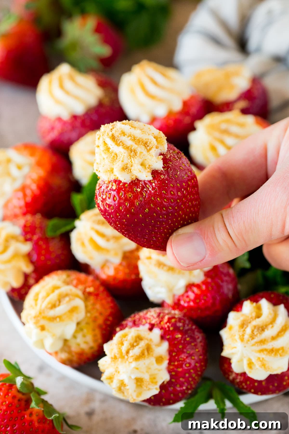 Strawberry Cheesecake Delights 6 A hand reaching for a cheesecake stuffed strawberry garnished with fresh mint from a plate, emphasizing the irresistible appeal of the dessert.