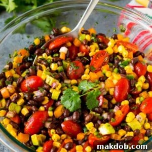 A bowl of black bean salad with a serving spoon in it.