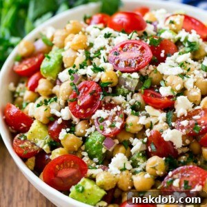A bowl of chickpea salad with tomatoes, cucumber, avocado, feta cheese and herbs.